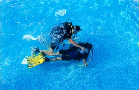 Deux plongeurs s'entraînent dans une piscine, un instructeur aide un élève