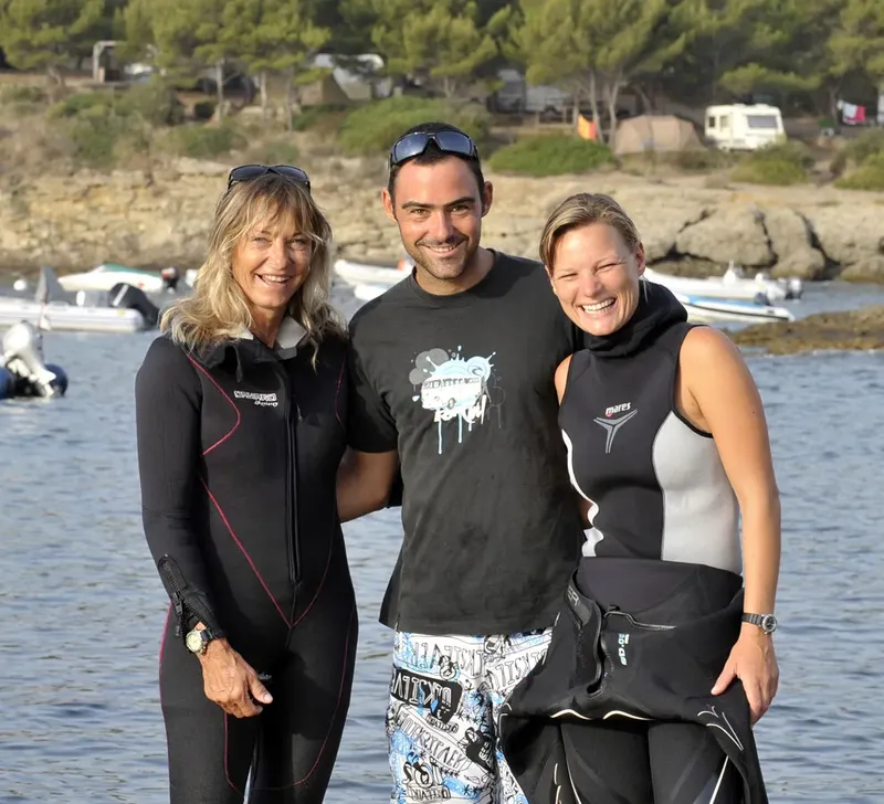 Trois personnes souriantes en tenue de plongée près de la mer