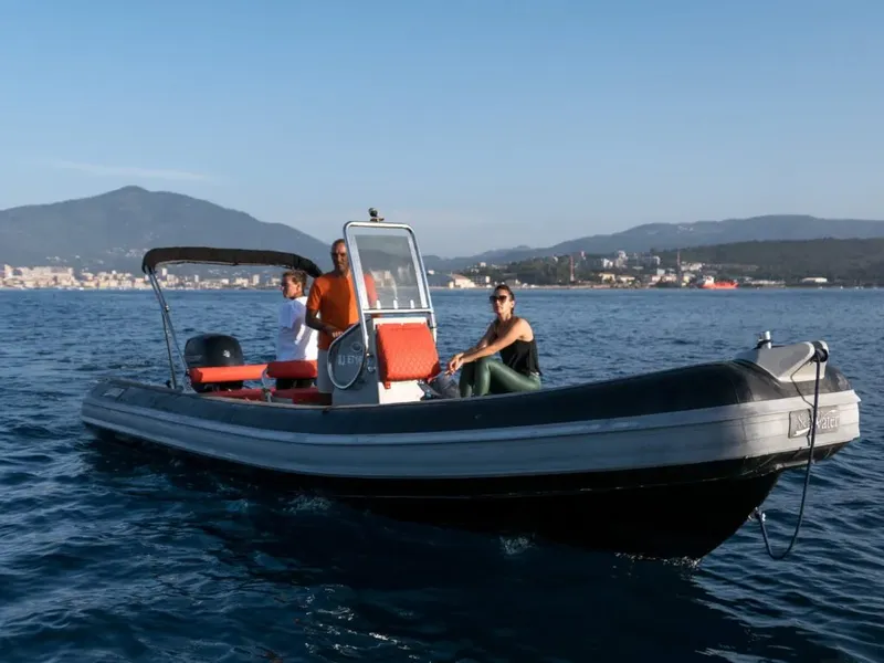 Trois personnes à bord d'un semi-rigide en mer, paysage côtier
