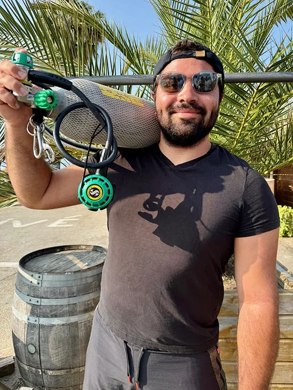 Plongeur souriant portant une bouteille et un détendeur sur son épaule