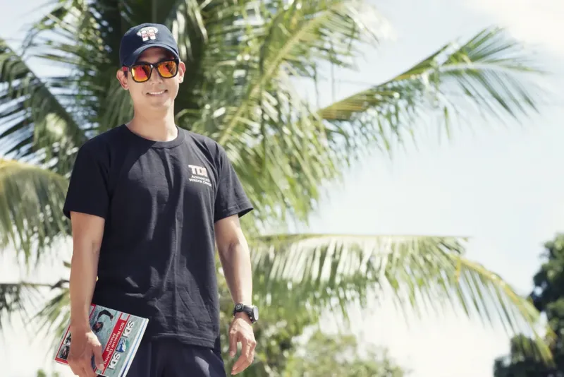 Un homme souriant porte un t-shirt noir et des lunettes de soleil