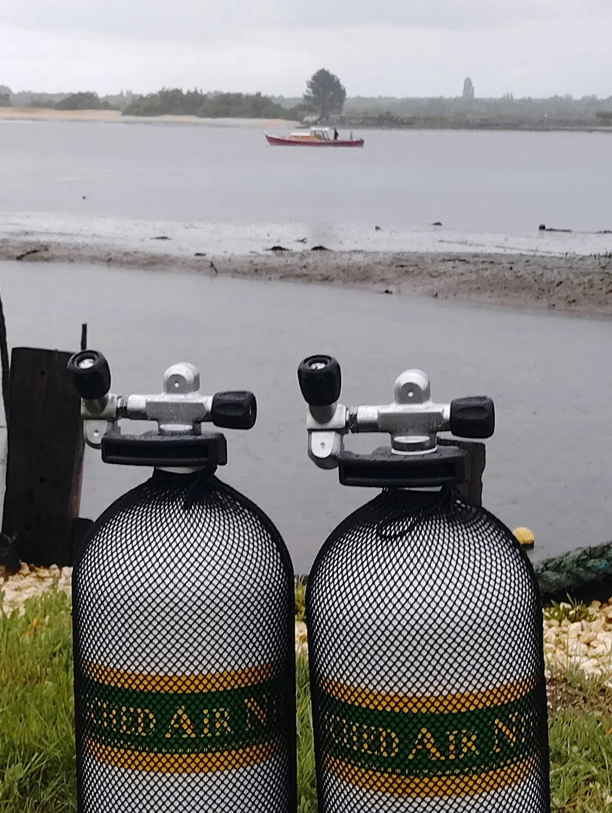 Deux bouteilles de plongée au premier plan, un bateau au loin