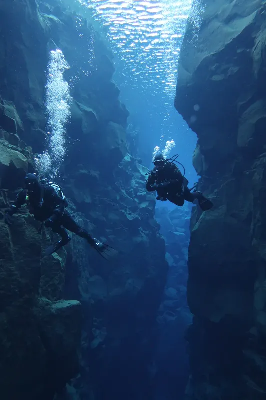 Deux plongeurs explorent une fissure rocheuse sous-marine, bulles remontant