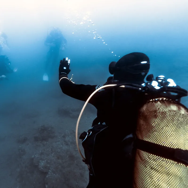 Plongeur en combinaison noire explore les fonds marins, bras levé