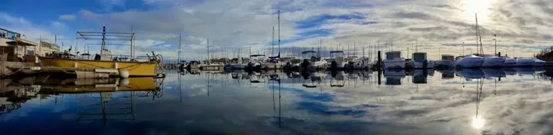 Port de plaisance ensoleillé avec bateaux à quai et reflets dans l'eau