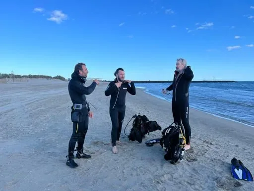 Trois plongeurs en combinaison discutent sur une plage de sable