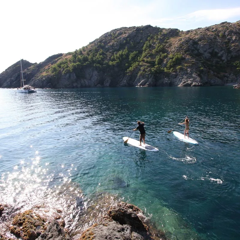 Deux personnes pratiquent le stand-up paddle dans une baie ensoleillée