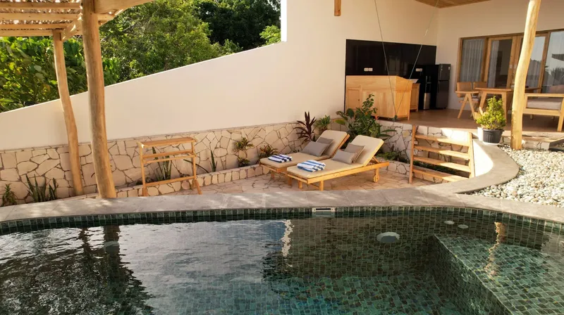 Terrasse avec transats, piscine et bâtiment blanc avec végétation tropicale