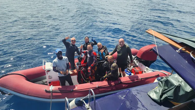 Groupe de plongeurs souriants à bord d'un bateau pneumatique rouge