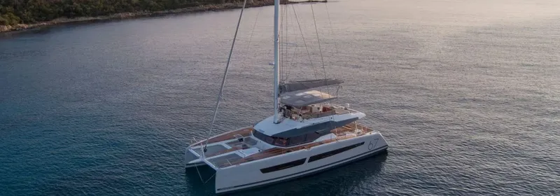 Catamaran blanc naviguant sur une mer calme au coucher du soleil