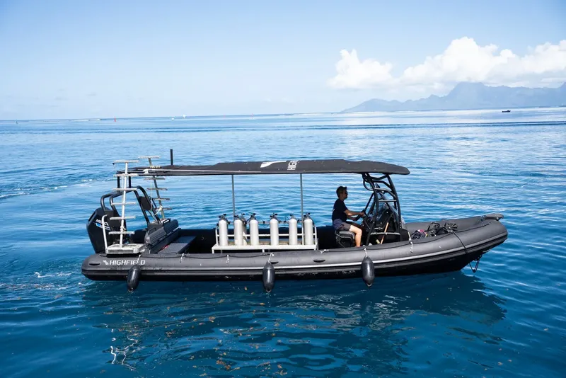Bateau semi-rigide noir en mer avec des bouteilles de plongée et un pilote