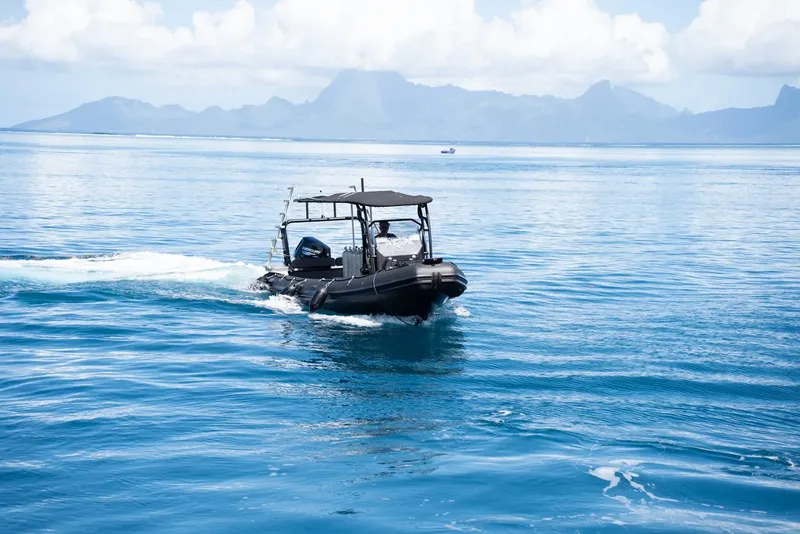 Bateau semi-rigide noir navigue sur une mer bleue avec des montagnes