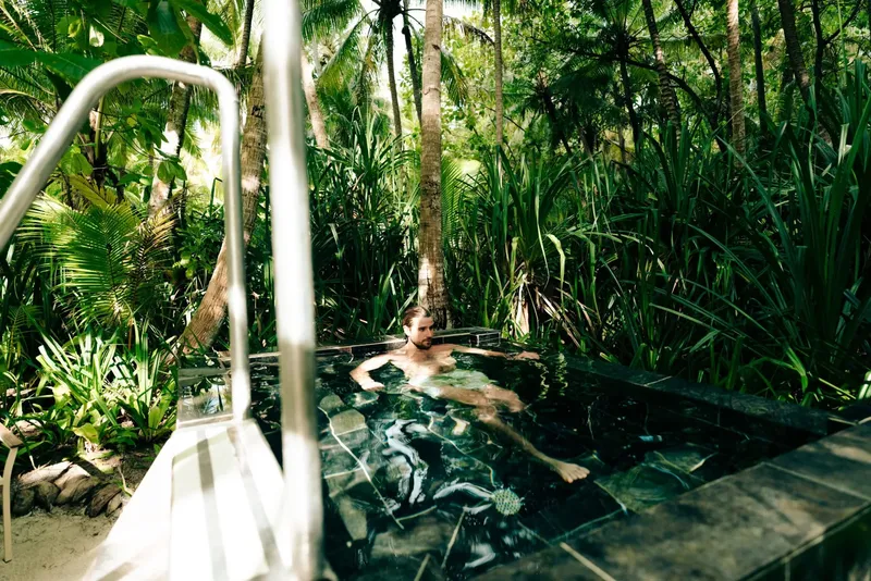 Un homme se relaxe dans une piscine naturelle entourée de végétation tropicale
