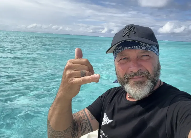 Homme souriant fait le signe 'shaka' en mer turquoise