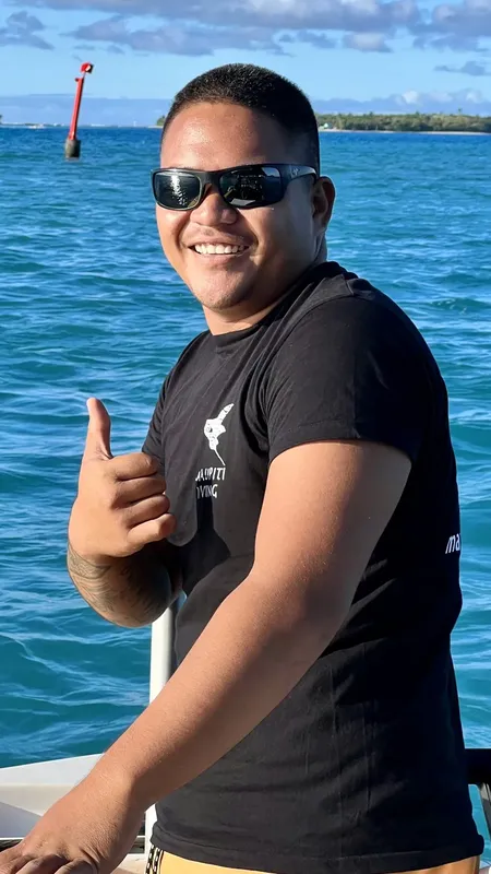 Homme souriant sur un bateau, pouce levé, mer turquoise en arrière-plan