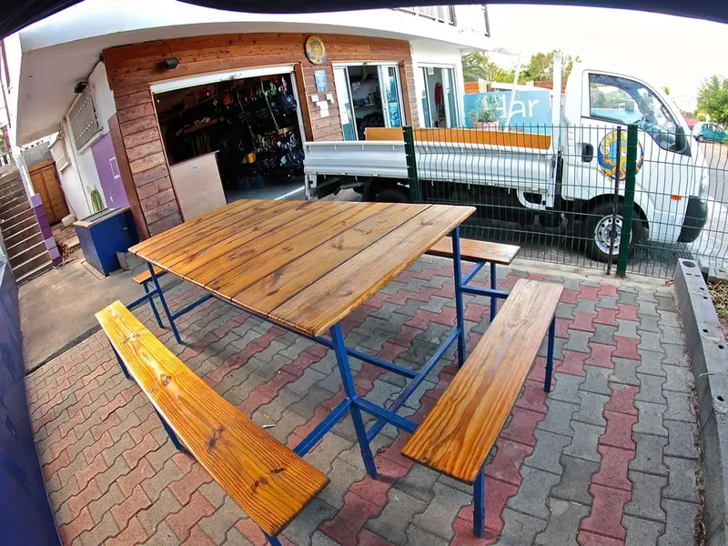 Table en bois et bancs devant un local de plongée et un camion