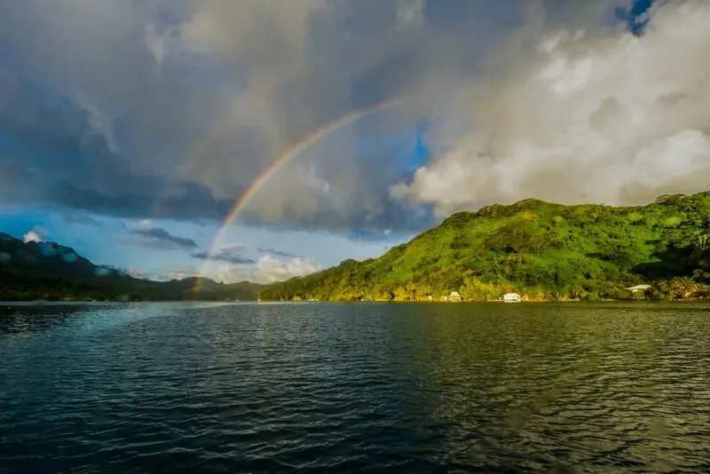 Paysage marin avec arc-en-ciel, montagnes verdoyantes et bateau au loin