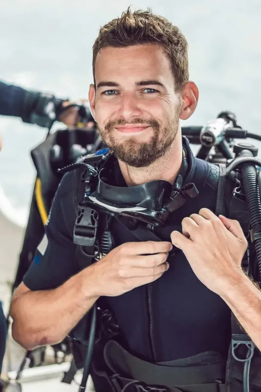 Plongeur souriant, équipé, tenant son détendeur, regardant la caméra