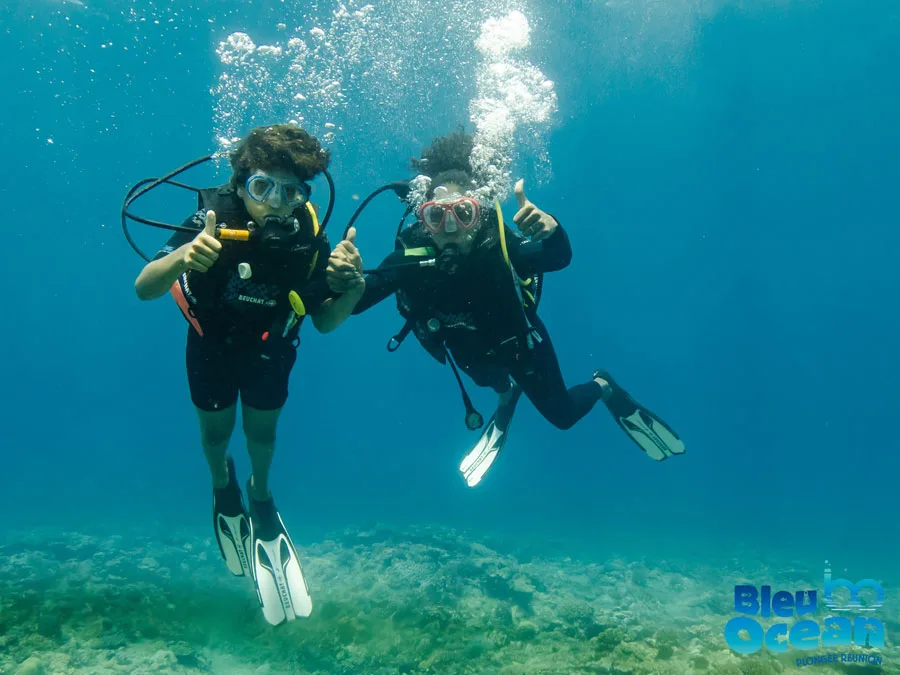 Deux plongeurs souriants, équipés, explorent un milieu aquatique bleu clair