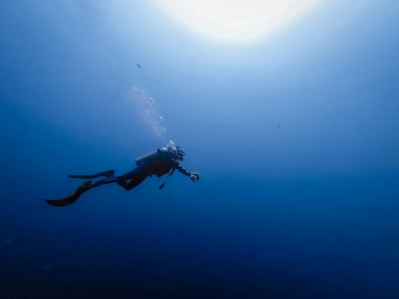 Plongeur en scaphandre nageant dans l'eau bleue sous les rayons du soleil