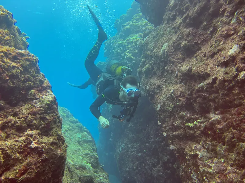 Plongeur explorant une fissure rocheuse sous-marine avec son équipement