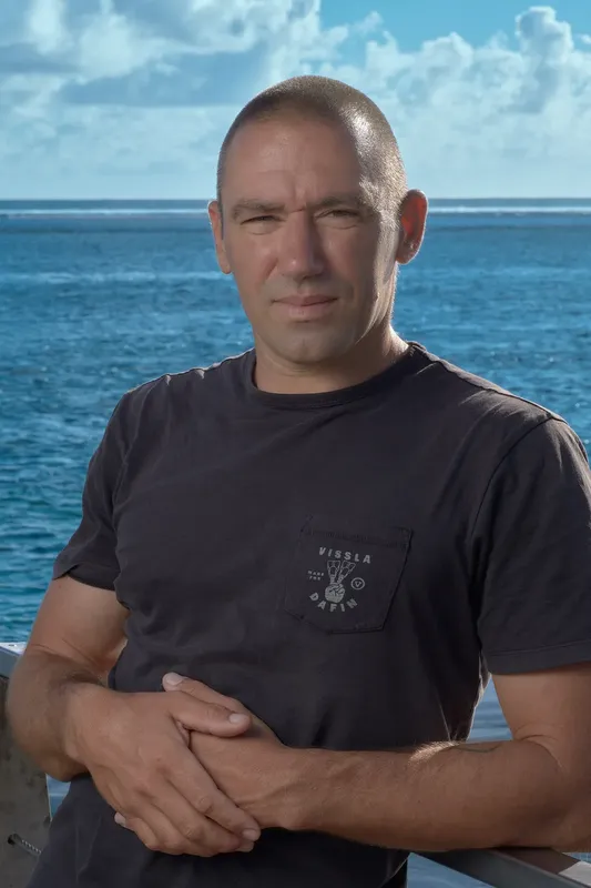 Homme souriant, torse nu, les bras croisés, devant la mer