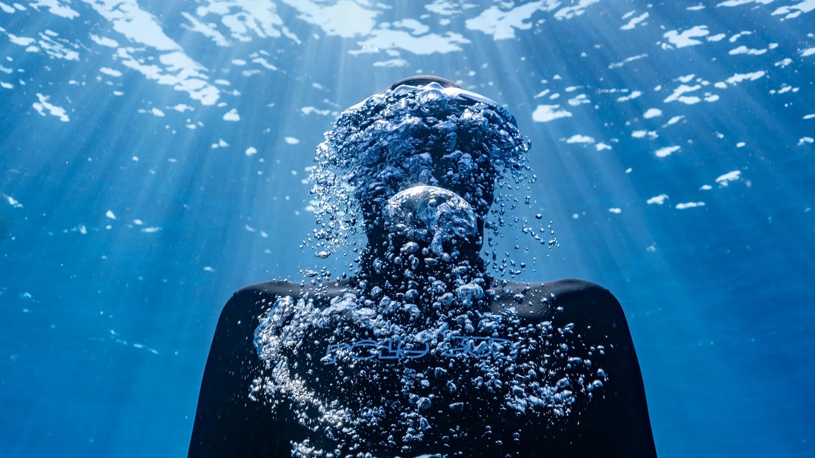 Plongeur en apnée entouré de bulles, lumière filtrant à travers l'eau