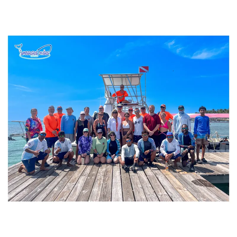 Groupe de plongeurs souriants posent devant un bateau sur un ponton