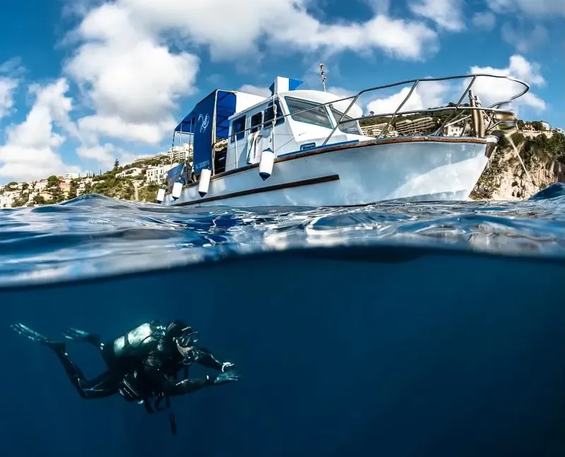 Plongeur en combinaison explore les fonds marins sous un bateau blanc