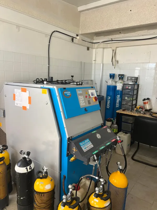 Compresseur de plongée bleu et bouteilles noires dans un local technique