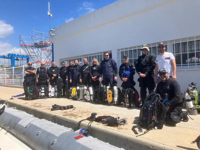 Groupe de plongeurs équipés devant un bâtiment blanc et un quai