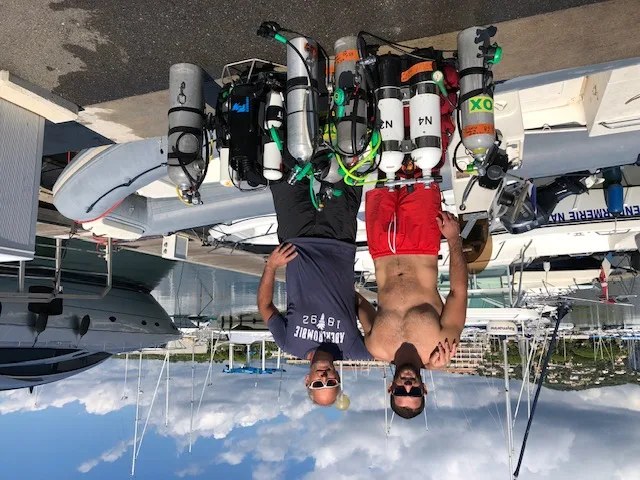 Deux hommes souriants posent avec des bouteilles de plongée sur un quai