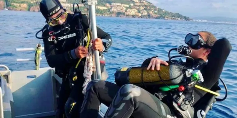 Deux plongeurs sur un bateau, l'un aide l'autre à s'équiper