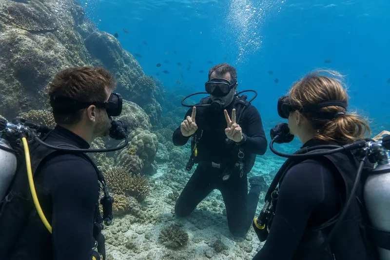 Trois plongeurs souriants interagissent sous l'eau avec des signes de la main