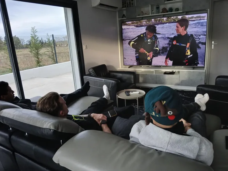 Des personnes se reposent sur des canapes devant un grand ecran de television