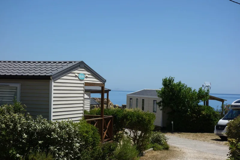 Mobil-homes blancs et bleus avec vue sur la mer et végétation