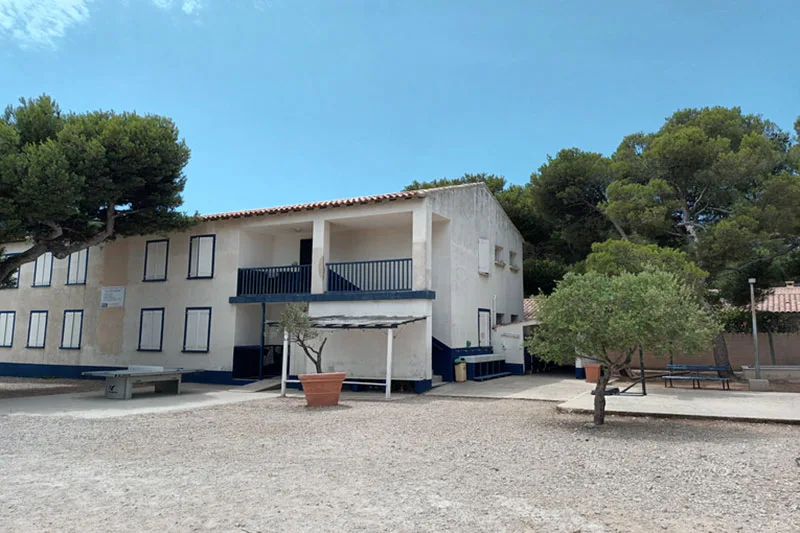 Bâtiment blanc à deux étages avec des arbres et un ciel bleu clair
