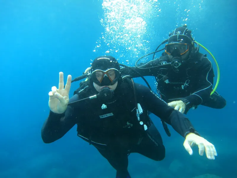 Deux plongeurs souriants font des signes de la main sous l'eau