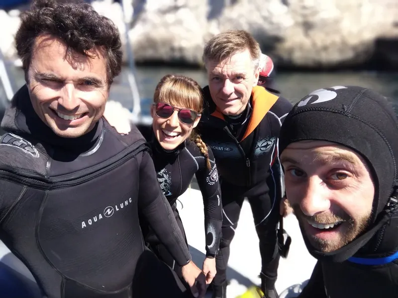 Quatre plongeurs souriants en combinaison, prêts pour une sortie en mer
