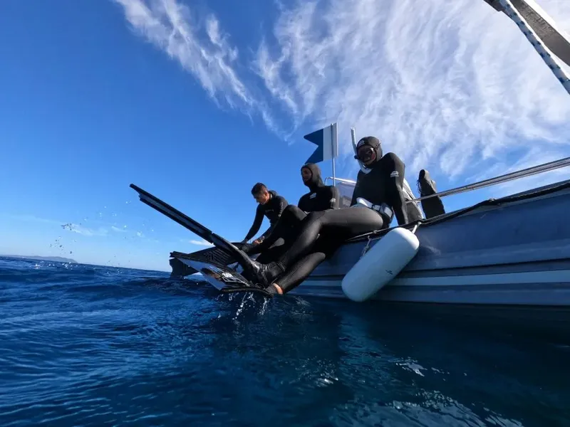 Trois personnes en combinaison de plongée s'apprêtent à entrer dans l'eau