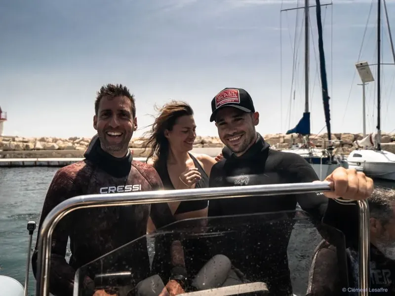 Trois personnes souriantes en combinaison de plongée sur un bateau