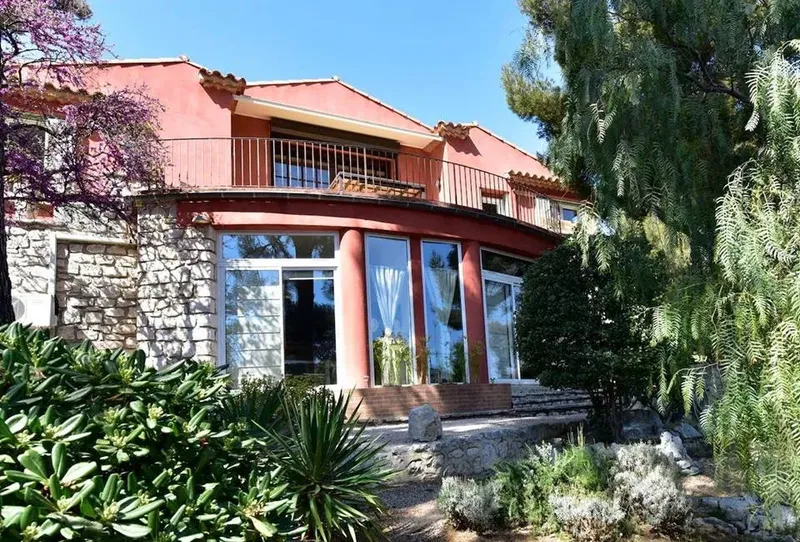 Bâtiment en pierre et bois avec balcon, entouré de végétation luxuriante