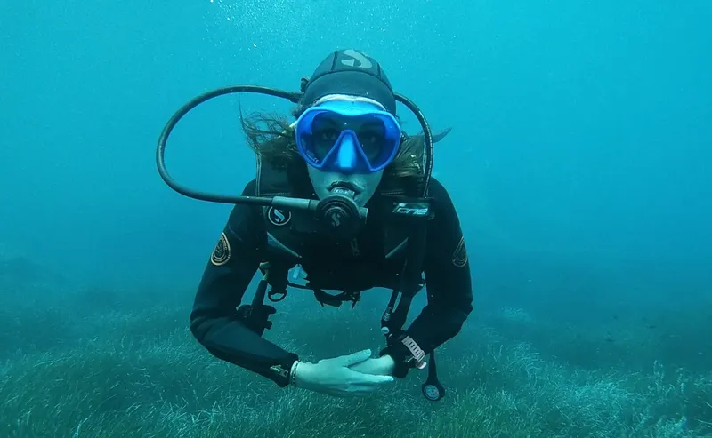 Plongeuse souriante en combinaison, masque et détendeur dans l'eau