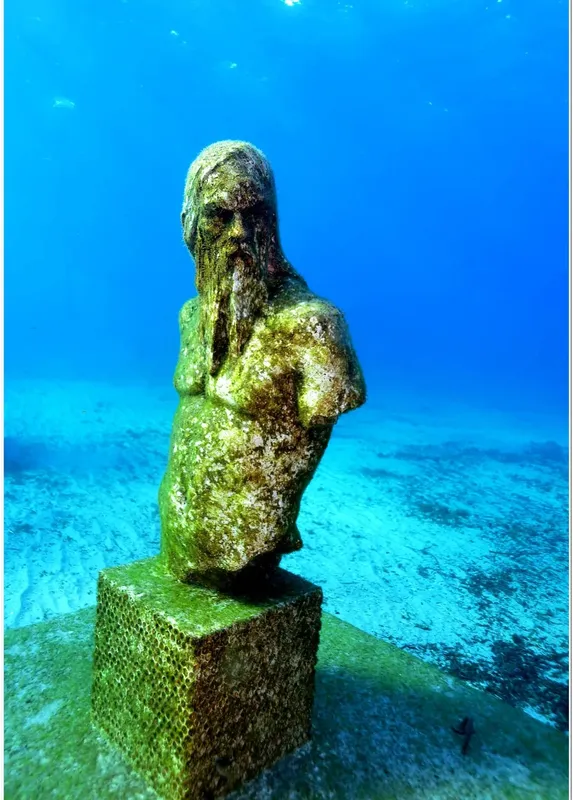 Buste de statue antique recouvert d'algues sous l'eau bleue