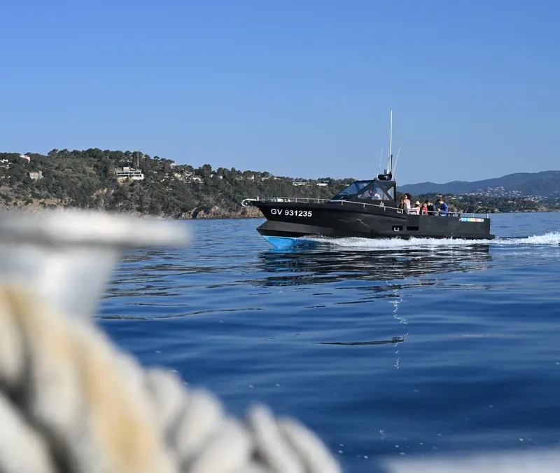 Bateau de plongée noir navigue sur une mer bleue calme et ensoleillée