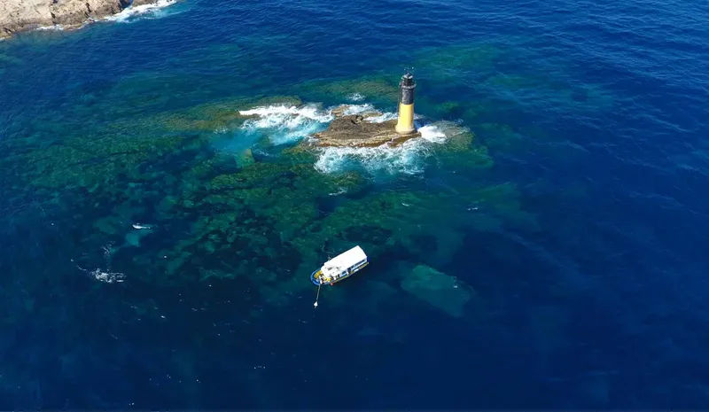 Phare sur un rocher entouré de mer bleue et un bateau
