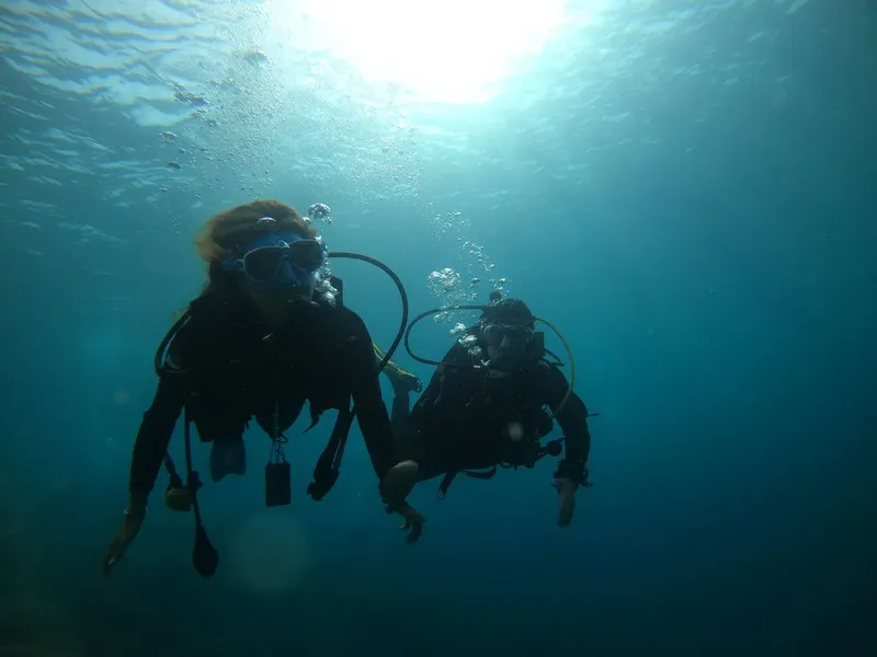 Deux plongeurs en combinaison explorent les profondeurs sous-marines, lumière filtrée