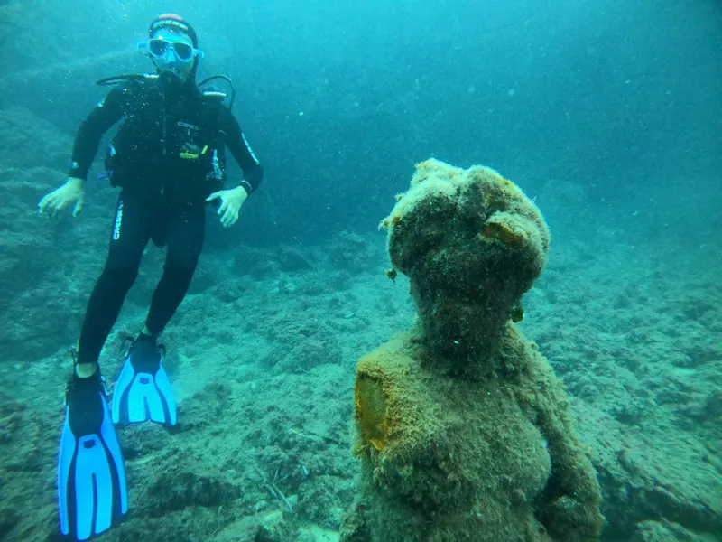 Plongeur explorant une sculpture sous-marine recouverte d'algues bleues
