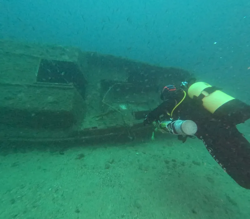 Plongeur explorant une épave sous-marine, visibilité moyenne, fond sableux