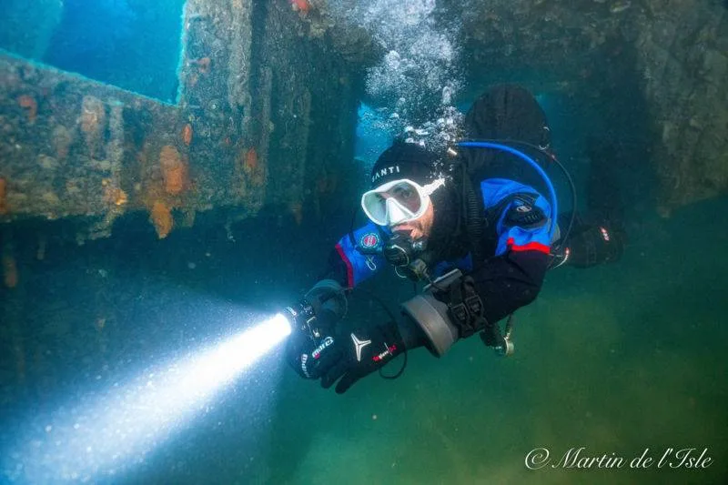 Plongeur avec lampe torche explore une épave sous-marine éclairée